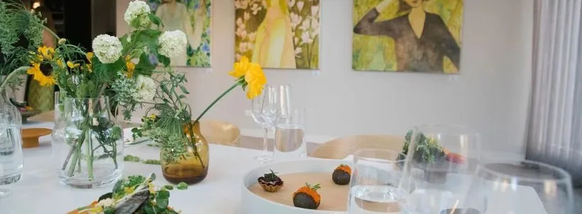 Flowers and dishes on a dining table beside artwork